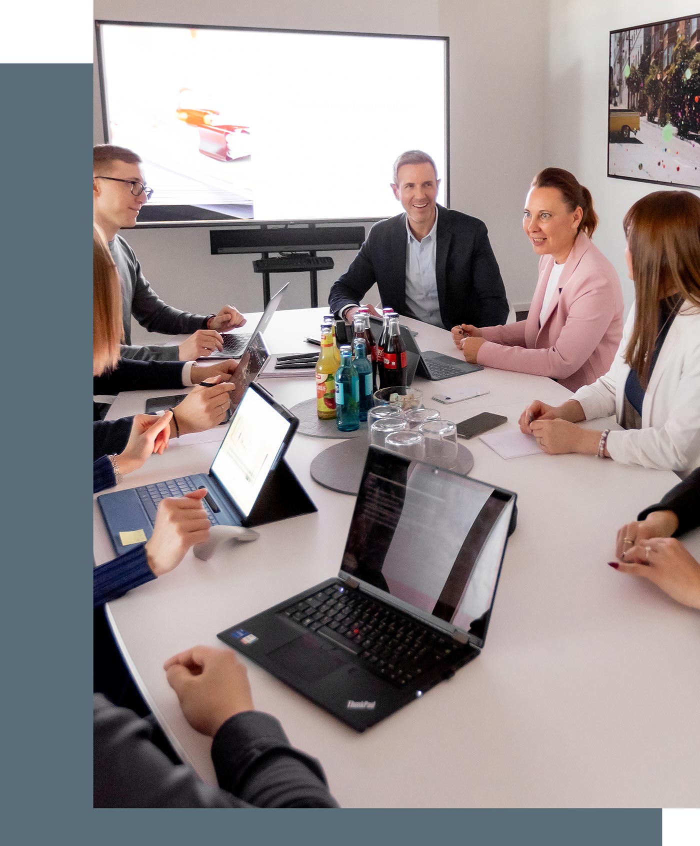Besprechung mit Mitarbeitern und Mandanten, auf dem Tisch stehen Laptops und Tablets sowie Getränke, ein Präsentationsmonitor in angeschaltet