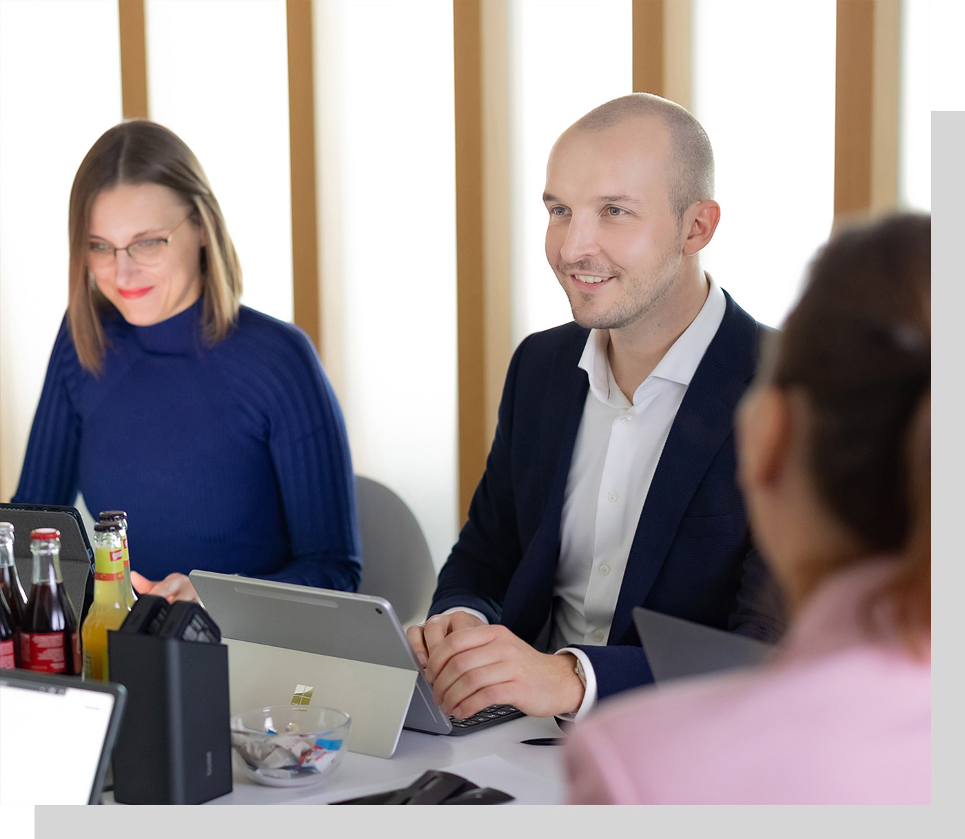 Mitarbeiter während einer Besprechung am Konferenztisch, Laptops und Tablet stehen auf dem Tisch, es wird sich angeregt und lächelnd unterhalten