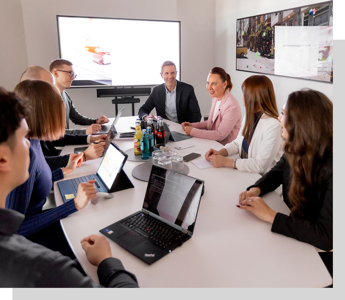 Besprechung mit Mitarbeitern und Mandanten, auf dem Tisch stehen Laptops und Tablets sowie Getränke, ein Präsentationsmonitor in angeschaltet