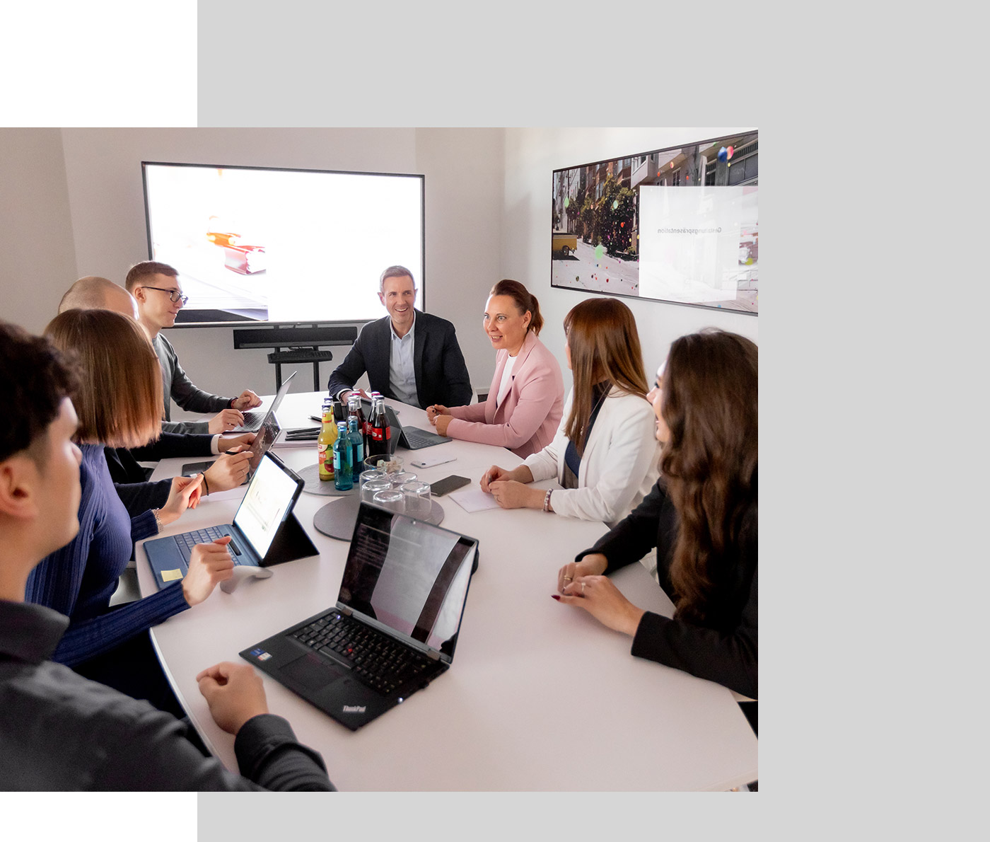 Besprechung mit Mitarbeitern und Mandanten, auf dem Tisch stehen Laptops und Tablets sowie Getränke, ein Präsentationsmonitor in angeschaltet
