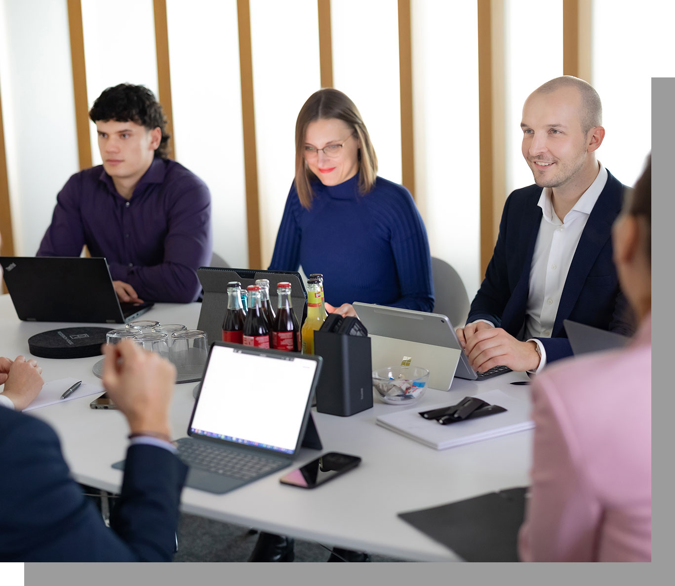 Mitarbeiter während einer Besprechung am Konferenztisch, Laptops und Tablet stehen auf dem Tisch, es wird sich angeregt und lächelnd unterhalten