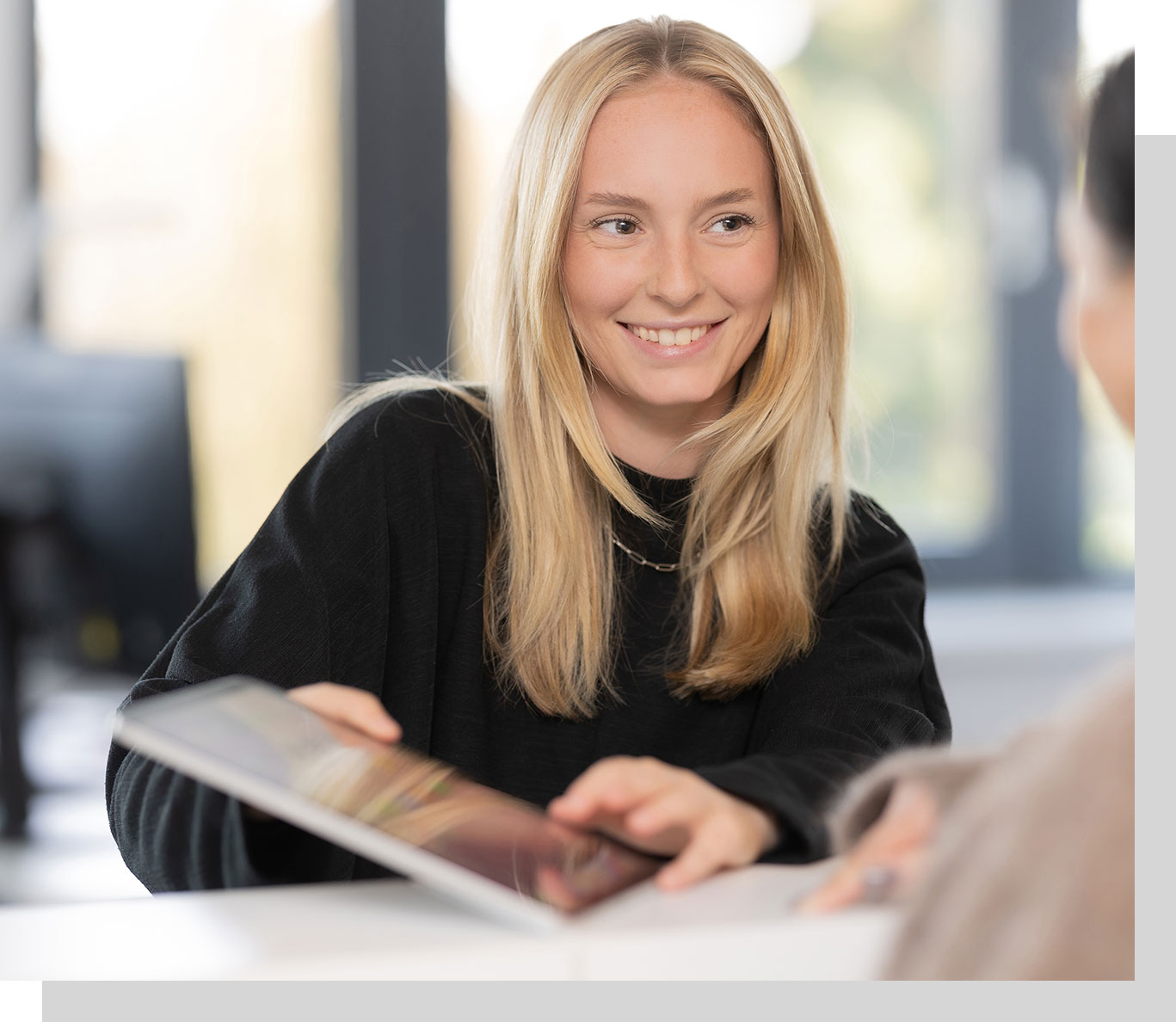 Eine Mitarbeiterin am Empfang zeigt einer Mandantin Unterlagen auf dem Tablet